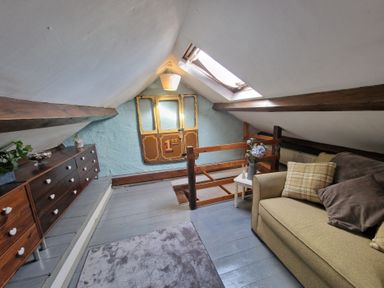 A small attic room with a sofa pillows wooden dresser skylight and decorative wall hanging at Quarry Cottage in Blaenau Ffestiniog