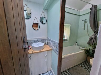 A bathroom with a wooden door round mirrors a sink and a bathtub with a shower at Quarry Cottage in Blaenau Ffestiniog