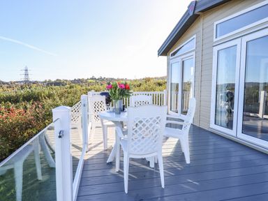 An outdoor deck with a white table and four white chairs with flowers on the table at Cherry Lodge in Teigngrace near Newton Abbot
