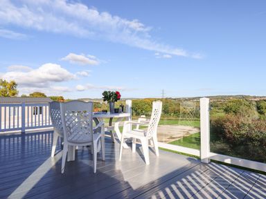 An outdoor deck with white chairs and a round table with flowers overlooking a green landscape at Cherry Lodge in Teigngrace near Newton Abbot