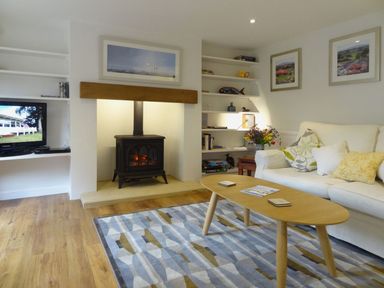 A living room with a wood stove fireplace a wooden coffee table white sofa and built-in shelves at Fiddlesticks Cottage in Beaminster