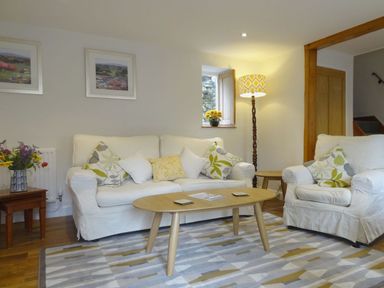 A living room with white sofas a wooden coffee table patterned cushions a floor lamp and flower arrangements at Fiddlesticks Cottage in Beaminster
