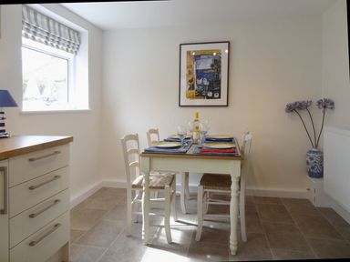 A dining area with a table set for four people next to a window and a blue and white vase with flowers at Fiddlesticks Cottage in Beaminster