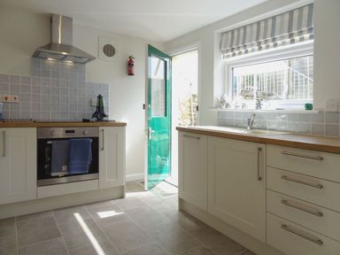 A kitchen with an oven stove range hood towels open green door and window with tea set at Fiddlesticks Cottage in Beaminster