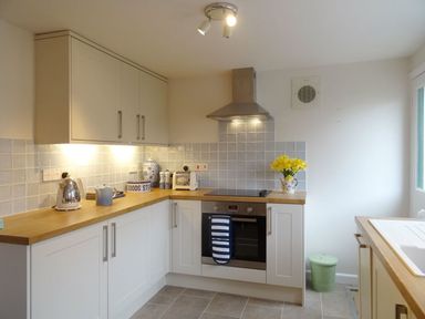 A kitchen with white cabinets wooden countertops a kettle toaster oven and flowers at Fiddlesticks Cottage in Beaminster