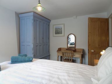 A bedroom with a bed, a blue wardrobe, a wooden desk with a mirror, and a wooden door at Fiddlesticks Cottage in Beaminster