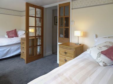 A bedroom with two single beds bedside tables with lamps and wooden framed glass doors at Fiddlesticks Cottage in Beaminster