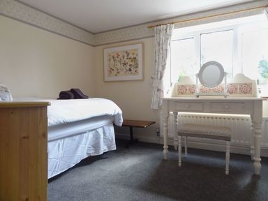 A bedroom with a single bed a small dressing table with a mirror and stool and a framed floral picture on the wall at Fiddlesticks Cottage in Beaminster