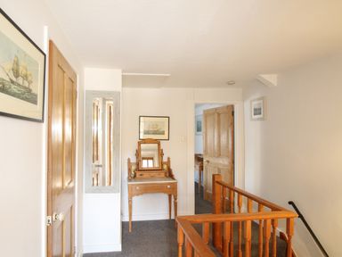A hallway with wooden doors a wooden vanity table with mirror and framed ship pictures at Fiddlesticks Cottage in Beaminster