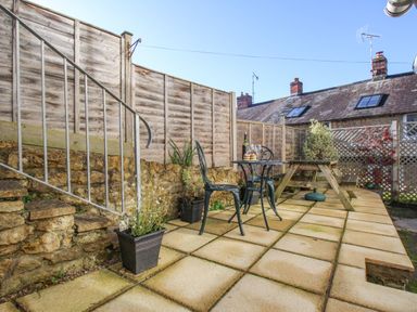 An outdoor patio with stone steps metal chairs and table wooden picnic bench and potted plants at Fiddlesticks Cottage in Beaminster
