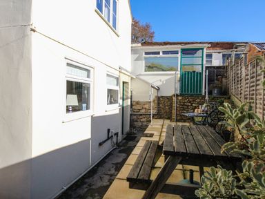 An outdoor patio area with a wooden picnic table and chairs adjacent to a white building at Fiddlesticks Cottage in Beaminster