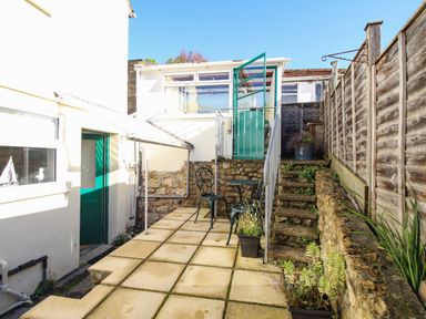 A small outdoor patio area with two metal chairs a table stone steps and potted plants at Fiddlesticks Cottage in Beaminster