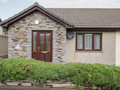 The exterior of a single-story house with a stone entrance door and a window with curtains at St Albans in Boscastle