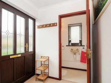 An entrance area with a wooden door a small shelving unit and a coat rack leading to a bathroom with a sink and a window at St Albans in Boscastle