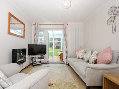 A living room with two sofas, a TV, a fireplace, a wall mirror, and glass doors leading to a garden at St Albans in Boscastle