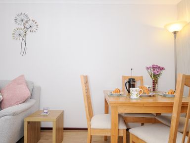 A dining area with wooden table and chairs set with croissants cups and a teapot beside a lamp and sofa at St Albans in Boscastle