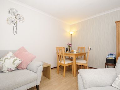 A dining area with a wooden table and four chairs next to grey sofas with cushions and a standing lamp at St Albans in Boscastle
