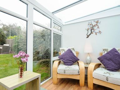 A sunroom with two armchairs with purple pillows a lamp on a side table and flowers on a wooden table at St Albans in Boscastle