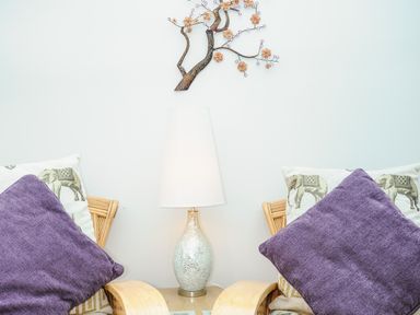 Two armchairs with purple and elephant print cushions a table with a lamp and wall art above at St Albans in Boscastle
