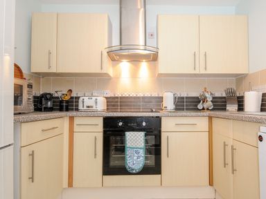 A kitchen with light wood cabinets a black oven a toaster kettle microwave and various utensils at St Albans in Boscastle