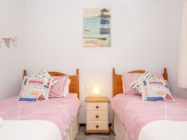 A bedroom with two single beds with pink bedspreads and pillows and a nightstand with a lit lamp between beds at St Albans in Boscastle