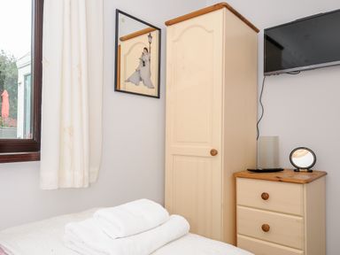 A bedroom corner with a wooden wardrobe a chest of drawers a mounted TV a window with curtains and folded towels on a bed at St Albans in Boscastle