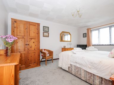 A bedroom with a wooden wardrobe a chair a dresser with a mirror and a bed with white linens at St Albans in Boscastle