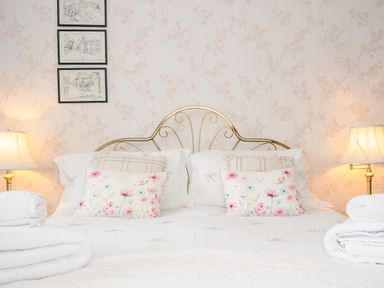 A bed with floral pillows and white linens with lamps on both sides and framed pictures on the wall at St Albans in Boscastle