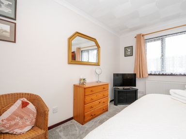 A bedroom with a wooden dresser and mirror a wicker chair with a cushion and a television on a black stand at St Albans in Boscastle