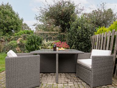 A patio area with four wicker armchairs around a glass table with a plate of croissants and a coffee pot surrounded by green plants and a wooden fence at St Albans in Boscastle