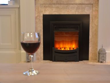 A glass of red wine on a table in front of a fireplace at Crabbe Corner in Aldeburgh