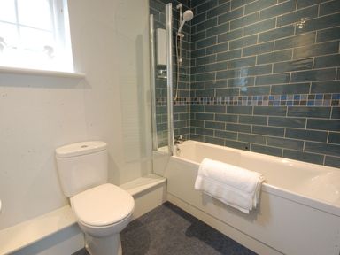 A bathroom with a toilet next to a bathtub with a shower and towel at Crabbe Corner in Aldeburgh
