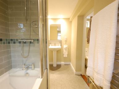 A bathroom with a bathtub shower combination a sink mirror and towel rack at Crabbe Corner in Aldeburgh