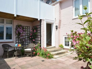 A patio area with a small table and two chairs and flowers along the walls at Crabbe Corner in Aldeburgh