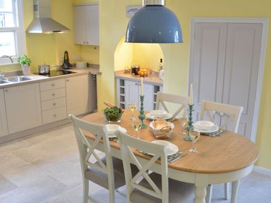 A kitchen with a dining table set for four people with plates glasses candles and bread at Crabbe Corner in Aldeburgh