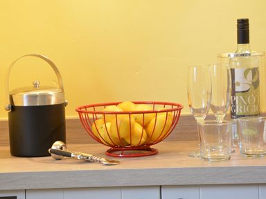A countertop with a black ice bucket a red basket of lemons a corkscrew a bottle of pinot grigio and empty glasses at Crabbe Corner in Aldeburgh