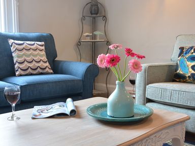 A living room with flowers in a vase on a table and two armchairs at Crabbe Corner in Aldeburgh