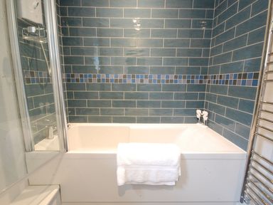 A bathroom with a bathtub and blue tiled walls at Crabbe Corner in Aldeburgh
