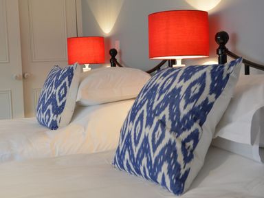 A bedroom with two beds each with blue patterned pillows and red lamps at Crabbe Corner in Aldeburgh