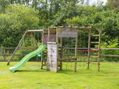 A play structure with a slide and swing in an outdoor play area at Branock, Tor Down Quarry in St Breward