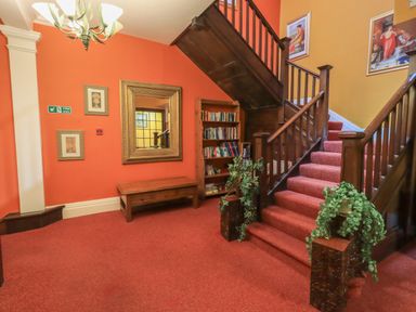 A staircase with red carpet next to a wooden bookshelf and a wooden table with a wall mirror at Peak View in Keswick