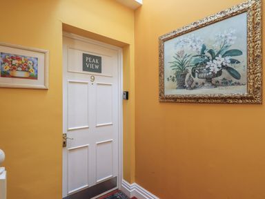 A hallway with a white door numbered nine and Peak View sign with yellow walls and flower paintings at Peak View in Keswick