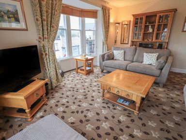 A living room with a gray sofa wooden coffee tables a TV on a wooden stand and floral carpet at Peak View in Keswick