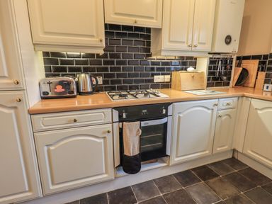 A kitchen with white cabinets a gas stove a black oven a toaster a kettle wooden countertops and black tiled backsplash at Peak View in Keswick