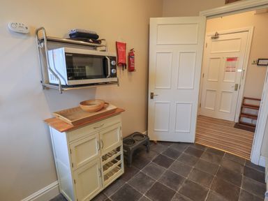 A small kitchen area with a microwave on a wall-mounted rack above a cabinet and an open door showing another room at Peak View in Keswick