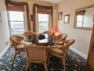 A dining area with a round glass table and six wicker chairs near two windows at Peak View in Keswick