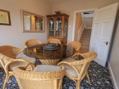 A dining room with a glass top table and wicker chairs a wooden cabinet a mirror on the wall and a staircase visible through an open door at Peak View in Keswick
