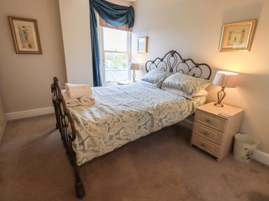 A bedroom with a double bed with patterned bedding a bedside table with a lamp and a window with blue curtains at Peak View in Keswick