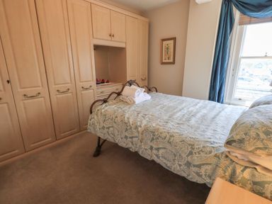 A bedroom with a bed covered with patterned bedding and folded towels on top next to built in closets and a window with blue curtains at Peak View in Keswick