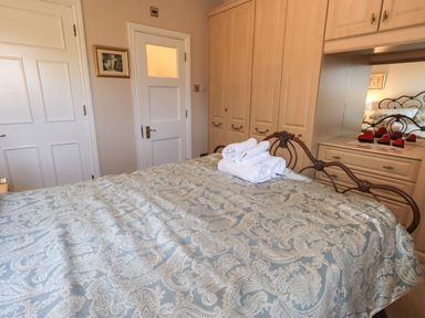 A bedroom with a patterned bedspread towels on bed built in wardrobes and a dresser with a mirror at Peak View in Keswick